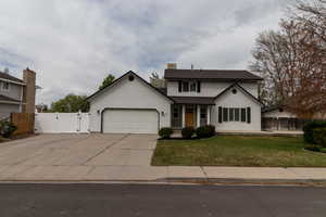Traditional-style home with a front lawn, a gate, concrete driveway, fence, and an attached garage