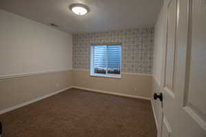 Empty room featuring baseboards, visible vents, dark colored carpet, and wallpapered walls