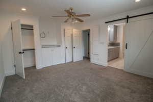 Unfurnished bedroom with ornamental molding, recessed lighting, light colored carpet, and a barn door