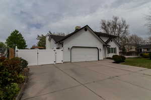 View of front facade with a chimney, a gate, fence, an attached garage, and driveway