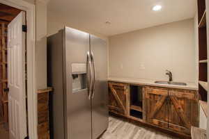 Kitchen featuring recessed lighting, light wood finished floors, a sink, light stone countertops, and stainless steel fridge