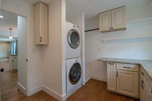 Clothes washing area with wood finished floors, stacked washer and dryer, baseboards, and laundry area