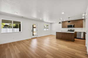 Kitchen with a kitchen island, open floor plan, hanging light fixtures, stainless steel appliances, and light wood-style flooring