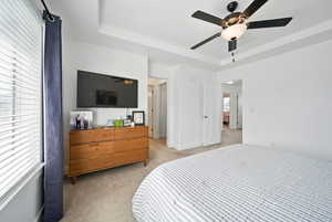 Bedroom featuring ceiling fan, light carpet, a tray ceiling, and visible vents
