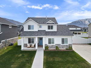 View of front of home featuring fence, a shingled roof, a front lawn, stone siding, and a mountain view