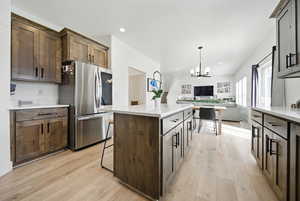 Kitchen with smart refrigerator, light wood-style floors, a kitchen island, open floor plan, and a notable chandelier