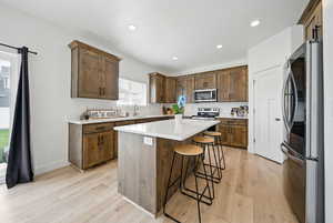 Kitchen featuring a center island, a sink, light wood-type flooring, a kitchen bar, and appliances with stainless steel finishes