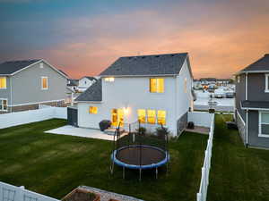 Back of property at dusk featuring a trampoline, a lawn, a fenced backyard, a patio, and stucco siding