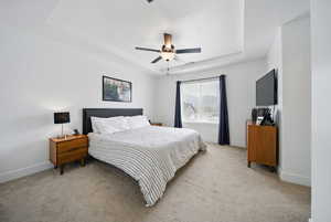 Bedroom with light carpet, a ceiling fan, baseboards, and a raised ceiling