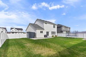 Rear view of property with a patio area, a fenced backyard, a yard, and a trampoline