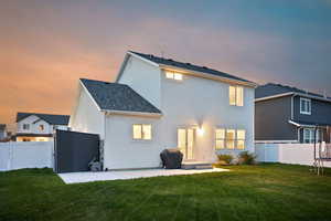 Back of property at dusk with stucco siding, french doors, a fenced backyard, and a lawn