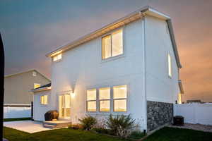 Back of house at dusk with fence, a yard, cooling unit, a patio, and stucco siding