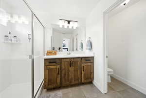 Bathroom with tile patterned floors, toilet, vanity, baseboards, and a stall shower