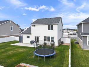 Rear view of house with a trampoline, a lawn, a fenced backyard, and a patio