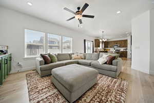 Living room with baseboards, recessed lighting, light wood-type flooring, and ceiling fan with notable chandelier
