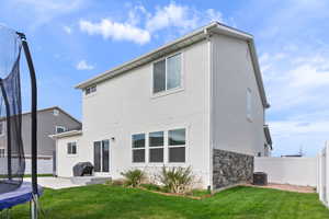 Back of property with a trampoline, stone siding, fence, a yard, and stucco siding