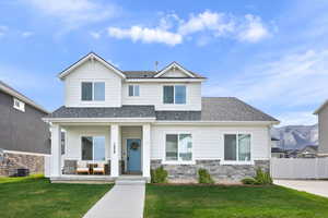 Craftsman-style home with roof with shingles, a porch, stone siding, fence, and a front yard