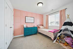 Bedroom with visible vents, light colored carpet, and a decorative wall