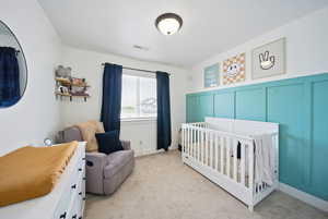 Bedroom with a nursery area, a decorative wall, carpet flooring, and visible vents