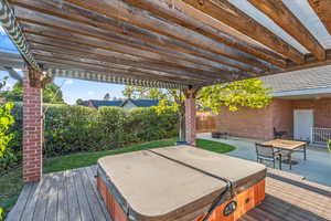 Wooden deck with a covered hot tub, a fenced backyard, and a patio