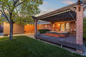Back of property at dusk with brick siding, a yard, hot tub deck surround, and fence