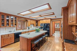 Kitchen with a kitchen island with sink, a sink, light wood-type flooring, a kitchen bar, and black appliances