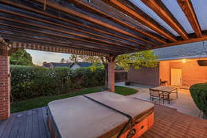 Deck at dusk featuring a covered hot tub, a fenced backyard, outdoor dining area, and a patio