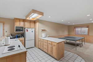 Kitchen with light countertops, a sink, white appliances, wainscoting, and a peninsula