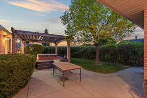 Patio terrace at dusk featuring a pergola, a lawn, and a hot tub