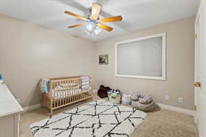 Bedroom with a nursery area, carpet, baseboards, and ceiling fan