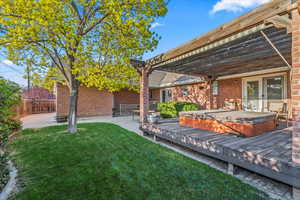 Back of property with fence, brick siding, a yard, a covered hot tub, and a patio