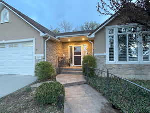 View of exterior entry with stone siding, an attached garage, and stucco siding