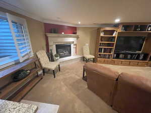 Carpeted living area featuring a tiled fireplace, recessed lighting, and ornamental molding