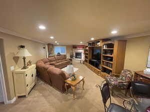 Living area with light carpet, recessed lighting, a fireplace with raised hearth, and crown molding