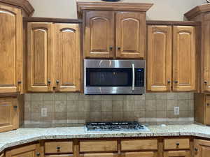 Kitchen with light stone counters, brown cabinets, appliances with stainless steel finishes, and decorative backsplash