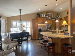 Kitchen featuring dark wood-style flooring, a sink, a breakfast bar, lofted ceiling, and appliances with stainless steel finishes