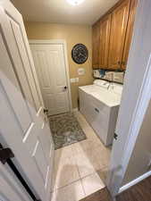 Laundry area with washer and clothes dryer, a textured ceiling, light tile patterned flooring, baseboards, and cabinet space