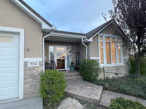 Property entrance with stucco siding, an attached garage, fence, and stone siding