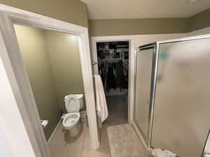 Full bath featuring a walk in closet, tile patterned flooring, toilet, and a stall shower