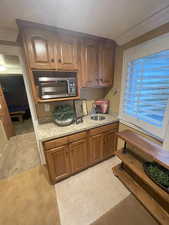 Kitchen featuring brown cabinets, light stone counters, light tile patterned floors, stainless steel microwave, and a sink