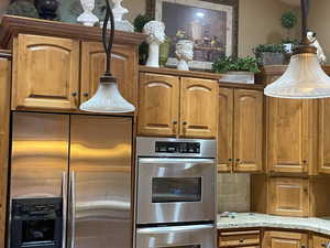 Kitchen with tasteful backsplash, light stone countertops, brown cabinetry, and stainless steel appliances