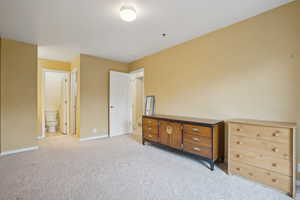 Bedroom featuring light carpet, ensuite bathroom, and baseboards