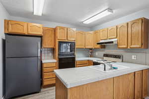 Kitchen with a peninsula, tasteful backsplash, under cabinet range hood, and black appliances
