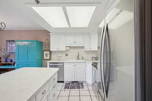 Kitchen with backsplash, a sink, light tile patterned flooring, appliances with stainless steel finishes, and white cabinetry