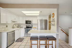 Kitchen with a kitchen breakfast bar, a sink, light tile patterned flooring, decorative backsplash, and appliances with stainless steel finishes