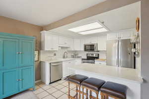 Kitchen featuring a kitchen breakfast bar, a sink, light tile patterned flooring, a peninsula, and appliances with stainless steel finishes