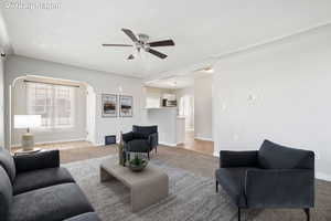 Living room featuring ceiling fan, arched walkways, baseboards, and light carpet