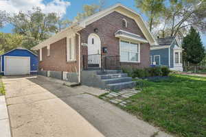 Bungalow featuring a detached garage, driveway, fence, brick siding, and an outdoor structure