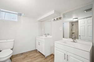 Bathroom with two vanities, wood finished floors, a sink, and visible vents