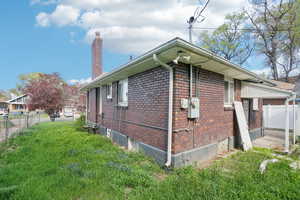 View of side of home featuring fence, a lawn, a chimney, and brick siding